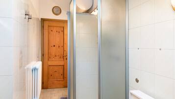 Een badkamer met een houten deur, een douchecabine van glas, een witte radiator en een toilet.