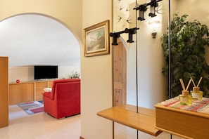 A modern living room with a red sofa, a television, a wooden table with decorative items, a large mirror, and a green plant. - Apartment 'Casa Vacanze Dal Castelin' with Mountain View, Balcony & Air Conditioning (Sondrio)