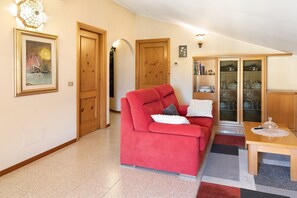Un soggiorno con un divano rosso, porte in legno, un tavolo da pranzo con piano in vetro e un armadio con ante in vetro.