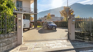 Área residencial murada com calçada pavimentada, um carro estacionado e um edifício com varanda.