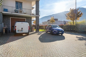 Zona residenziale con vialetto lastricato, un furgone bianco e un'auto blu parcheggiati di fronte a un edificio con un balcone.