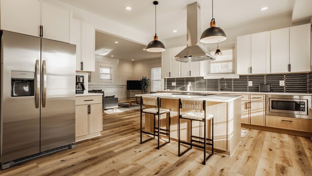 Una cocina moderna con electrodomésticos de acero inoxidable, suelo de madera e iluminación colgante.