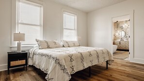 A bedroom with a bed, bedside table, lamp, and a view of the bathroom.