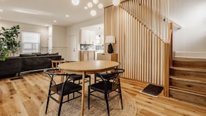 Una sala de estar moderna con una escalera de madera, un comedor con una mesa redonda y sillas, y una cocina al fondo.