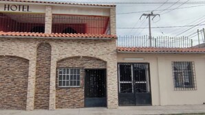 A two-story building with a sign reading "HOTEL" on the upper level. There are three arched doorways on the ground floor, and a small annex attached to the main building. - Hotel Destination (Cuatro Ciénegas)