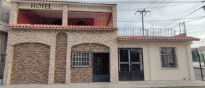 A two-story building with a sign reading "HOTEL" on the upper level. There are three arched doorways on the ground floor, and a small annex attached to the main building. - Hotel Destination (Cuatro Ciénegas)