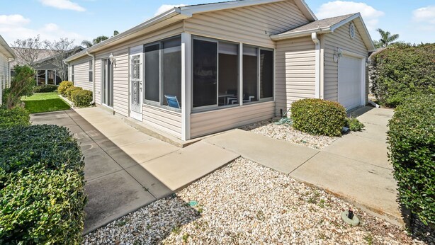 A single-story house with a covered porch, a garage, and a well-maintained garden with gravel pathways and trimmed bushes. - 2/2 Patio Villa in De La Vista (The Villages)