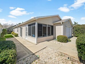 Een gelijkvloers huis met een overdekte veranda, een garage en een goed onderhouden tuin met grindpaden en bijgewerkte struiken.
