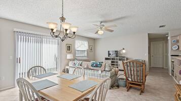 A dining area with a wooden table and chairs, a chandelier, and a ceiling fan.