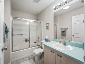 Een badkamer met een douchecabine van glas, een wit toilet, een wastafel met een lichtblauwe bladplank en een spiegel boven de wastafel.