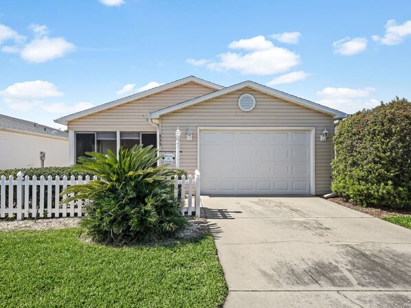 Een gelijkvloers huis met een garage, een witte picket fence en een verzorgd gazon.