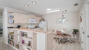A compact kitchen with a microwave, stove, and refrigerator. There is a dining area with a table and chairs, and a bookshelf filled with books and decorative items.