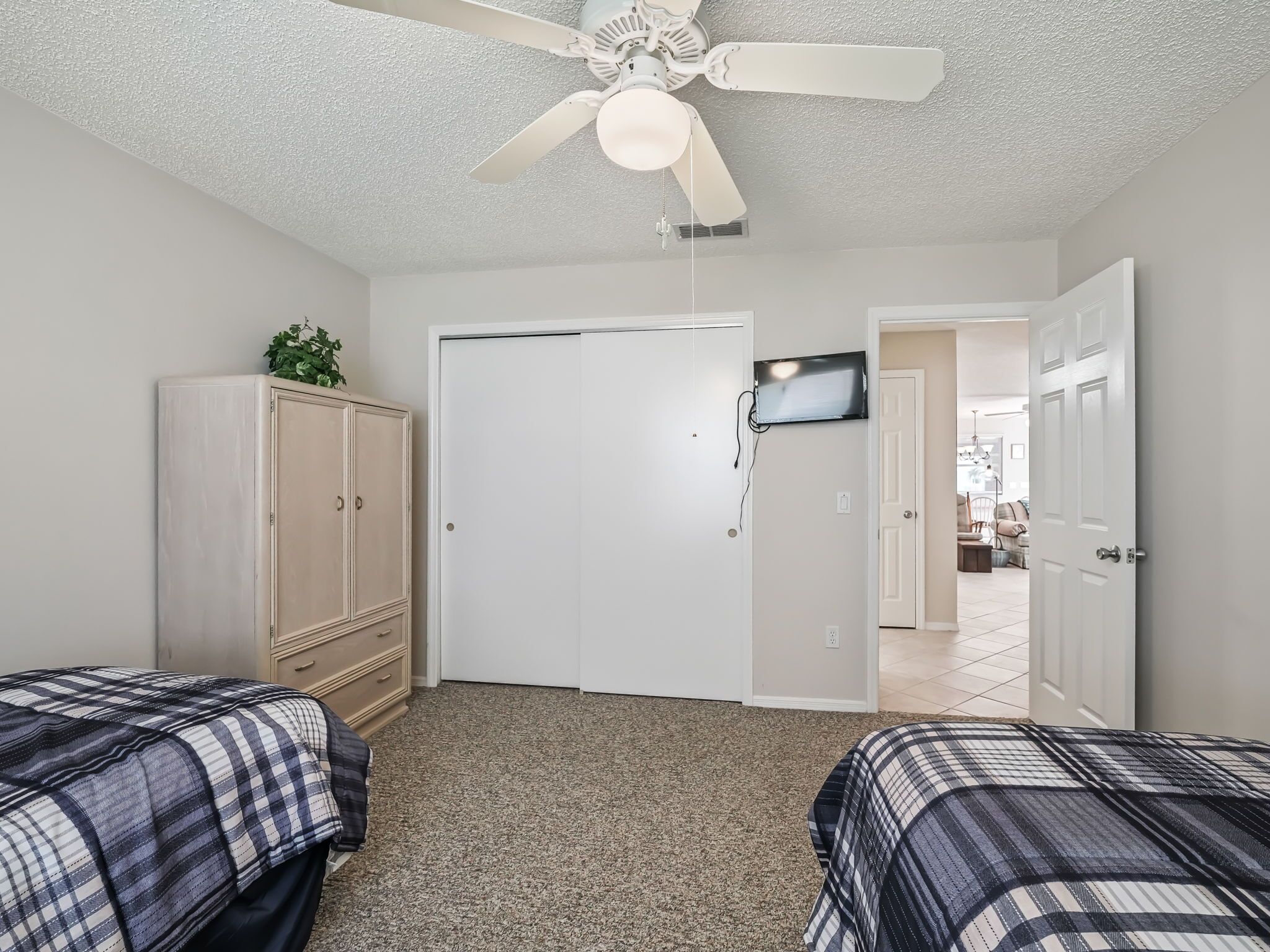 A bedroom with two beds, a ceiling fan, a TV, and a wardrobe.