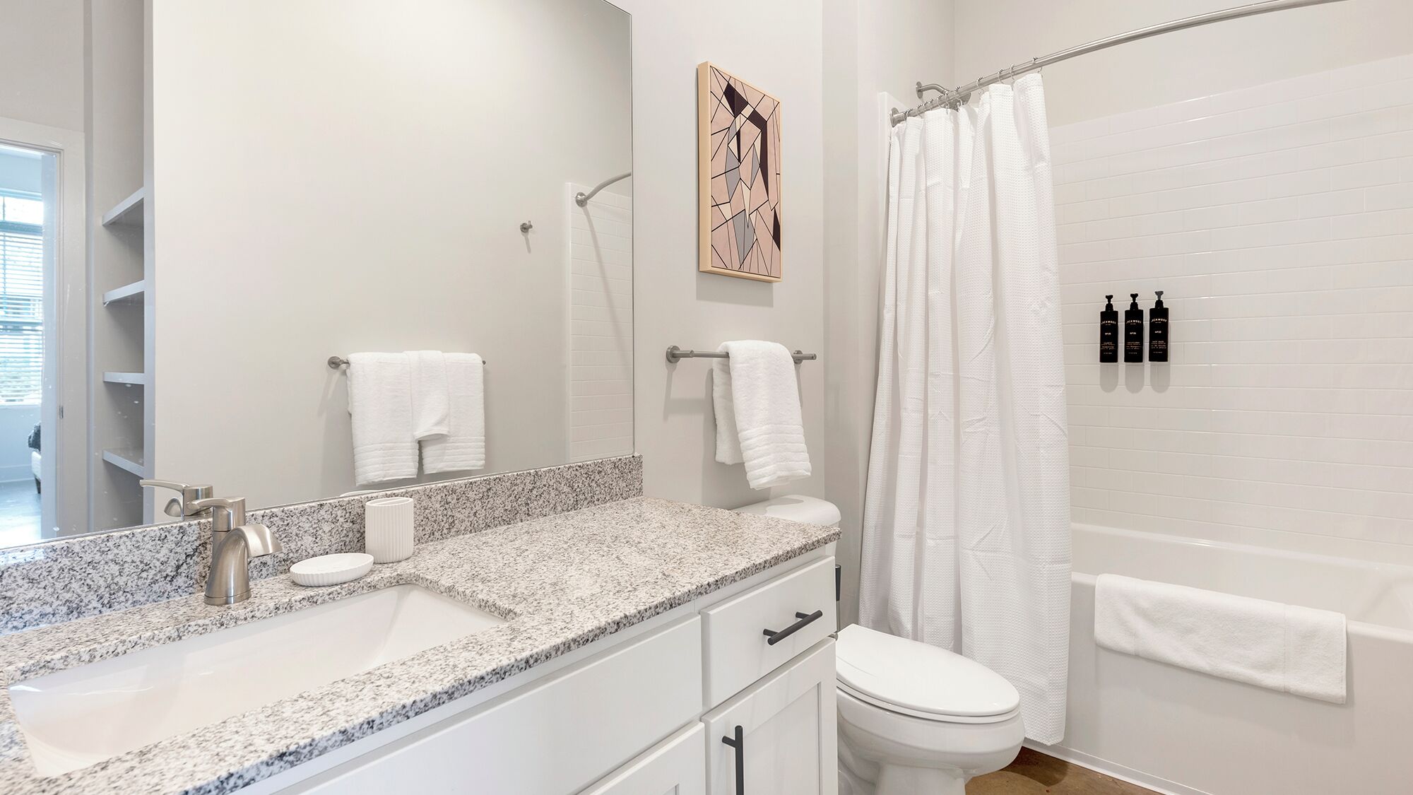 A bathroom with a granite countertop, a white toilet, a shower with a white curtain, and a towel rack with two towels.