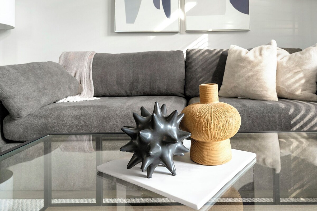 A modern living room with a glass coffee table, a grey sofa, and decorative items.