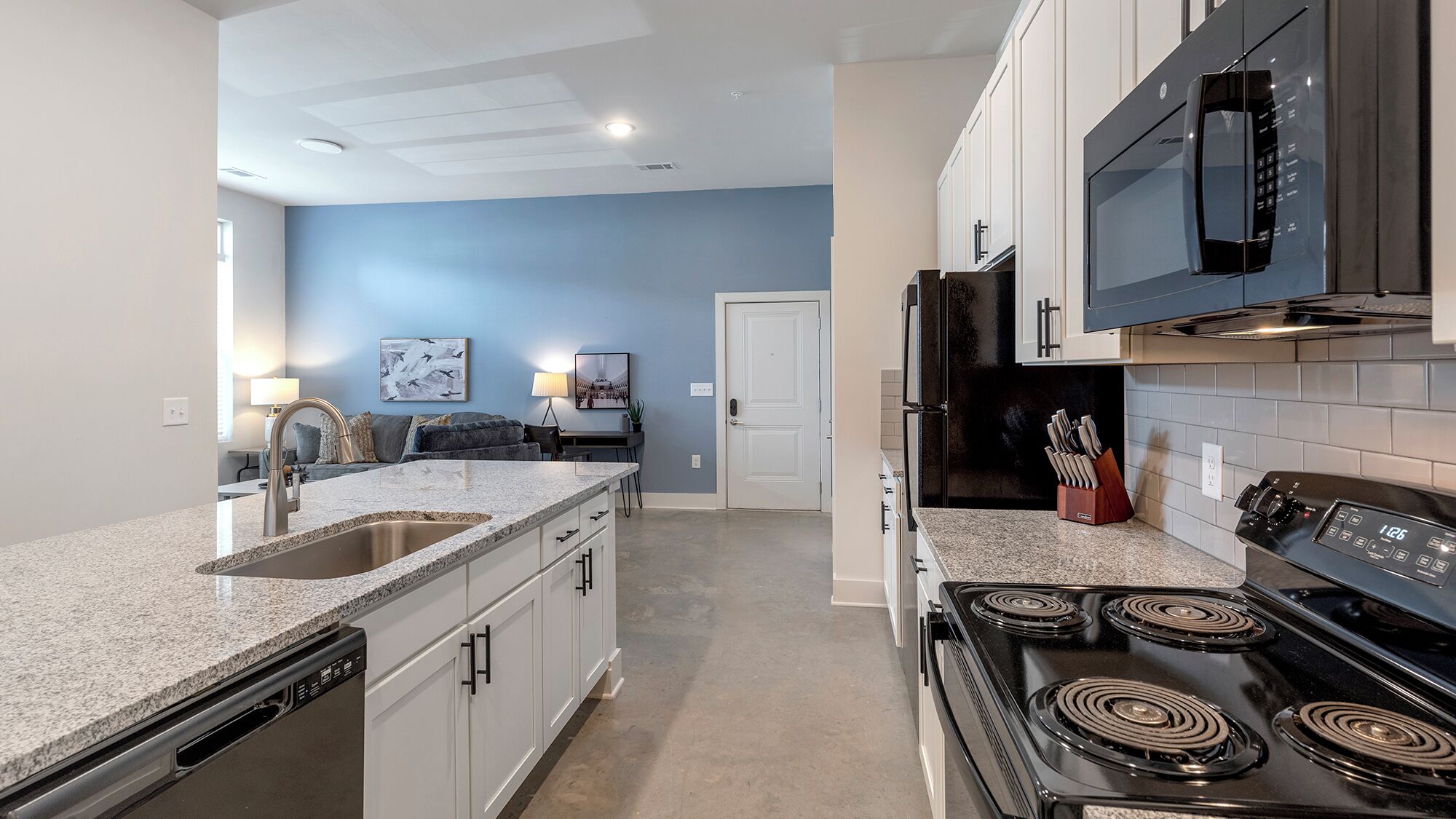 A modern kitchen with granite countertops, a black stove, and white cabinets.
