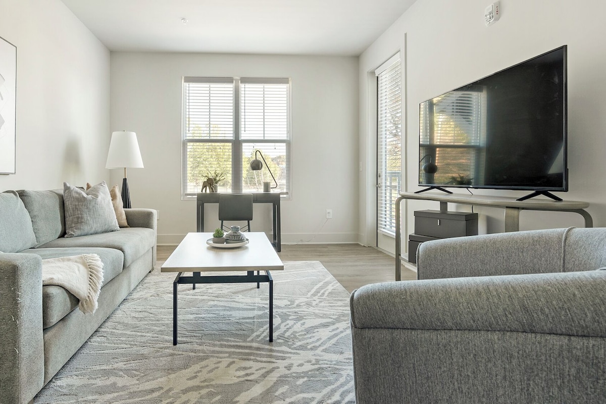 A modern living room with a grey sofa, a coffee table, and a TV on a stand.