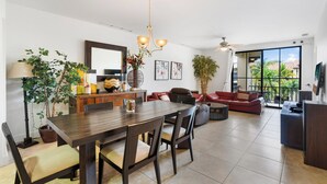 Un vaste espace dédié à la salle à manger, avec une table et des chaises en bois, un canapé rouge et une grande fenêtre offrant une vue sur les palmiers.