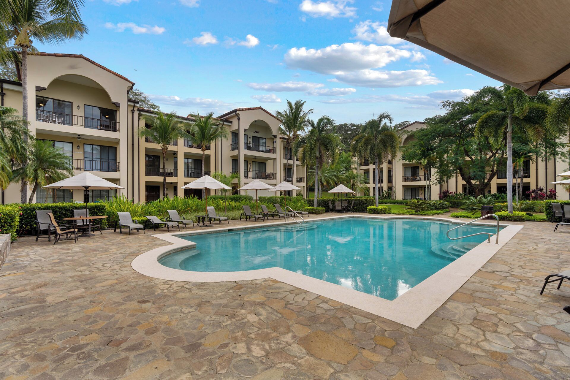 A pool area with lounge chairs and umbrellas, surrounded by a multi-story building with balconies.