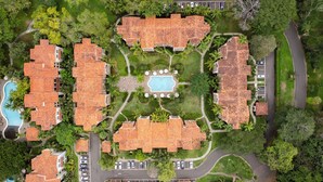 Vue aérienne d’un complexe hôtelier comprenant plusieurs bâtiments, une piscine centrale et de nombreux espaces verts.