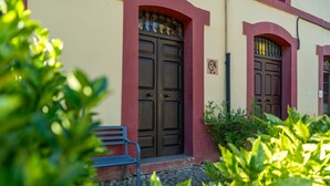 A building with two brown doors, a bench, and some greenery in the foreground.