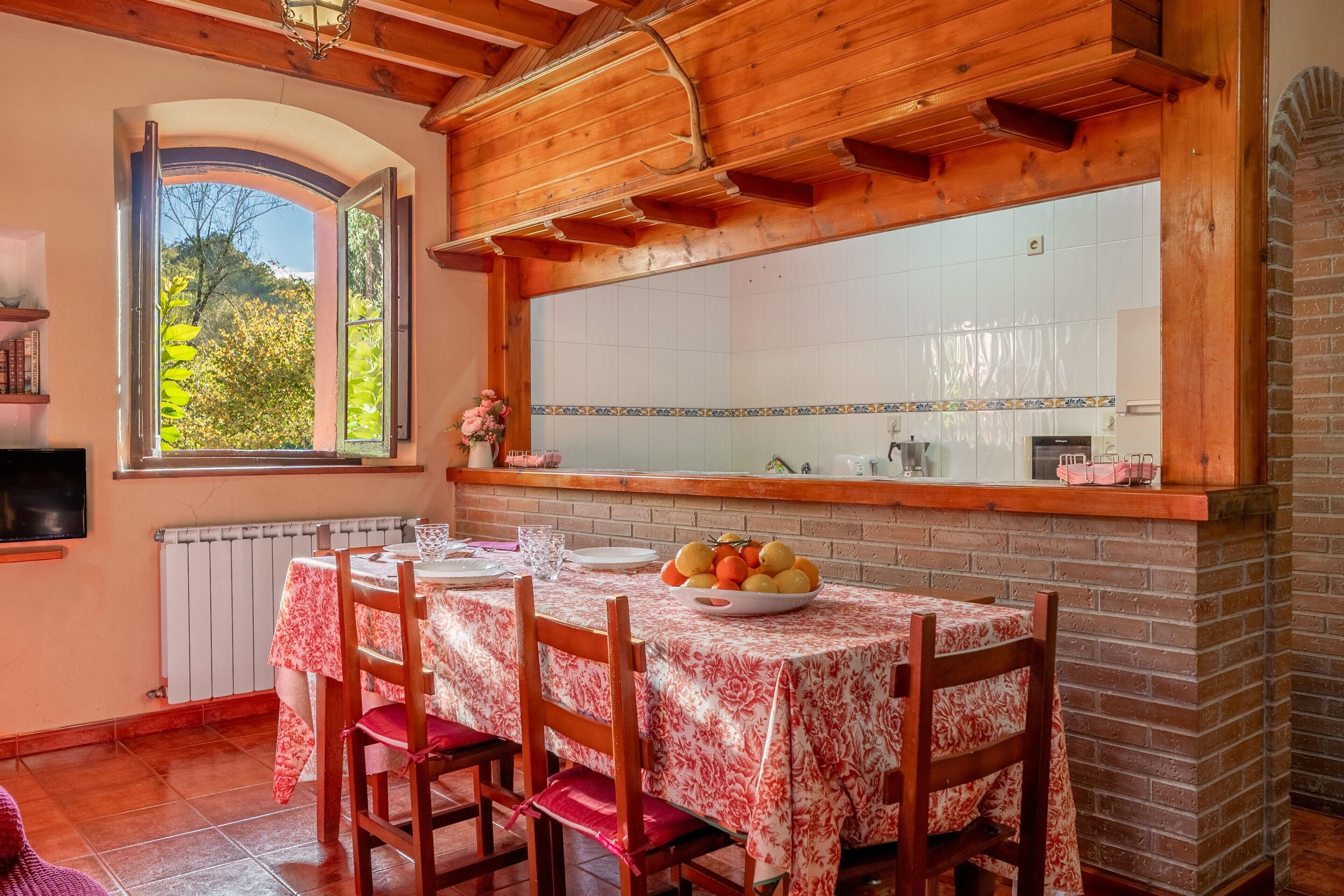 A dining area with a table set for four, a window with a view of trees, and a brick wall with a tiled backsplash.