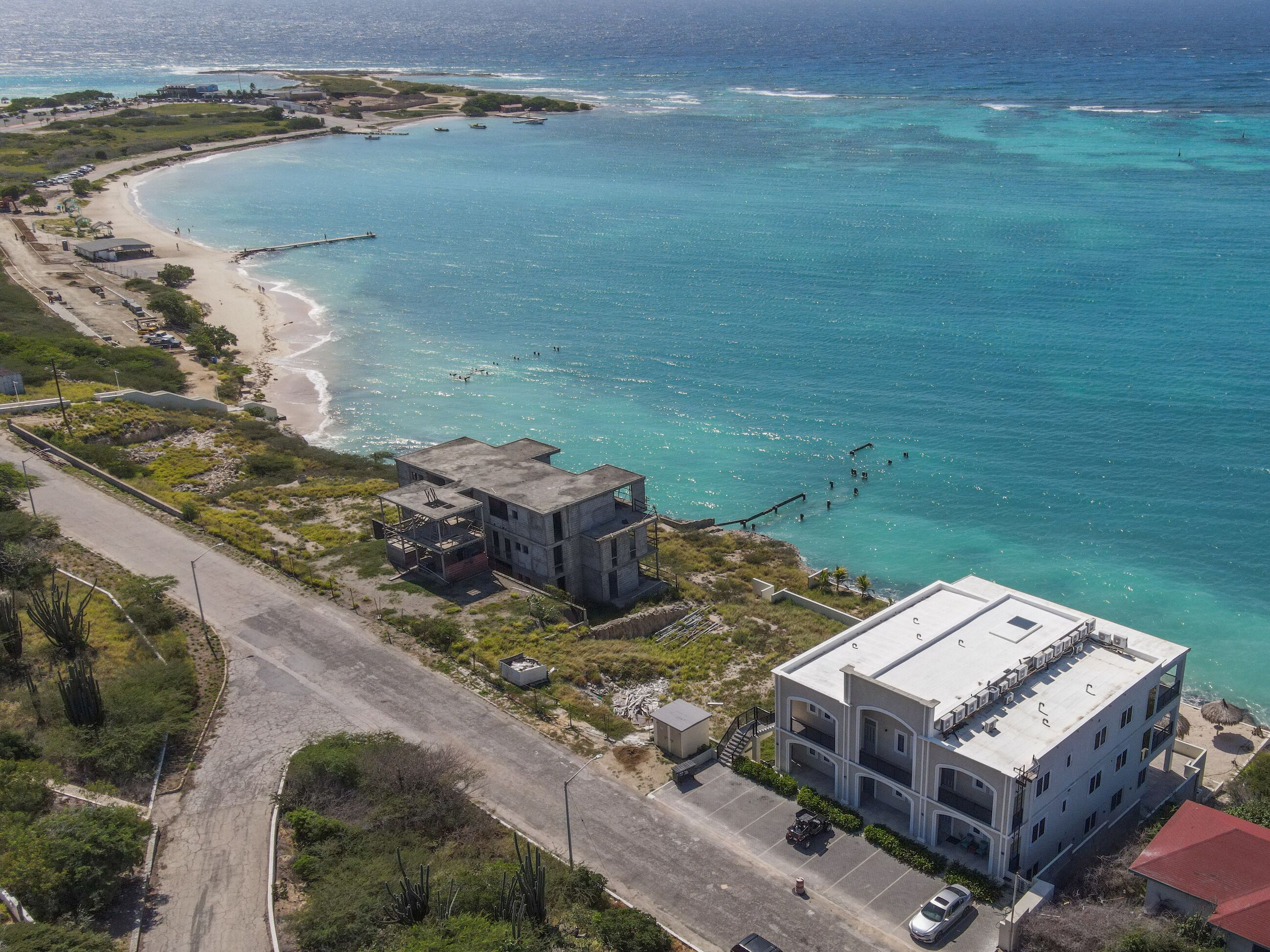 Vista aérea de una zona costera con un edificio grande, una playa y aguas azules cristalinas.