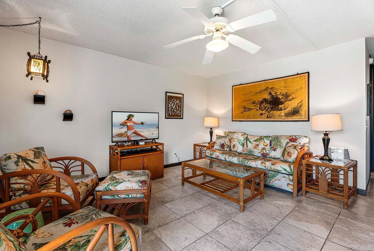 A living room with a television, sofa, chairs, and a ceiling fan.