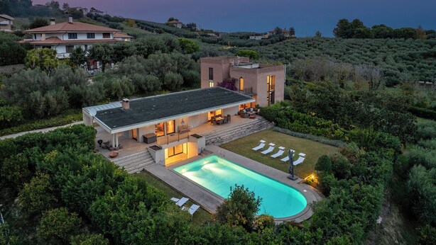 Ein modernes Haus mit Swimmingpool, umgeben von üppiger Vegetation und Blick auf das Meer.