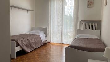 Una camera da letto con due letti singoli, pavimento in legno, un termosifone e una finestra con tende leggere.