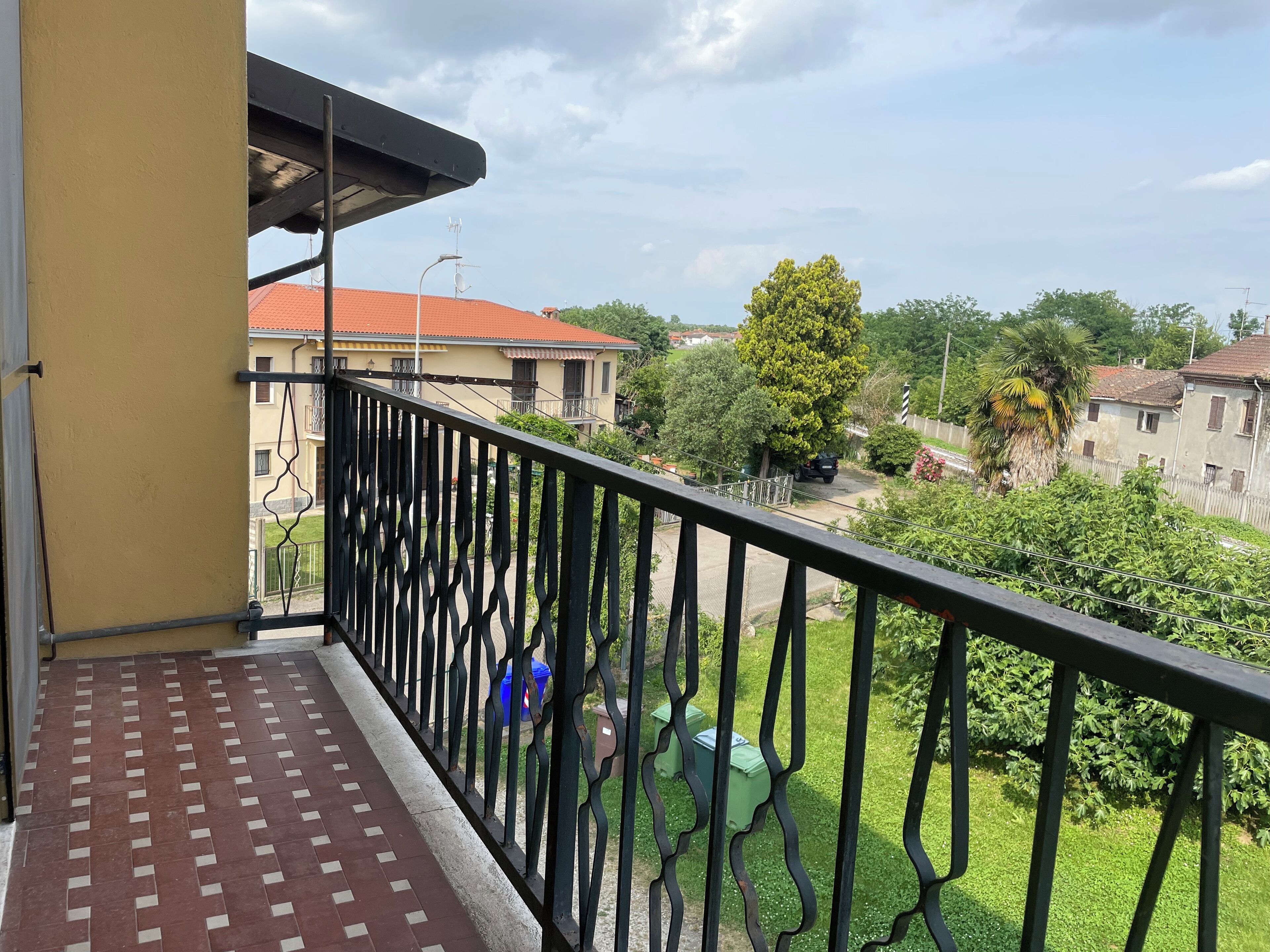 Un balcon doté d’un sol à motifs, d’une rambarde en métal et offrant une vue sur les bâtiments et la végétation environnants.