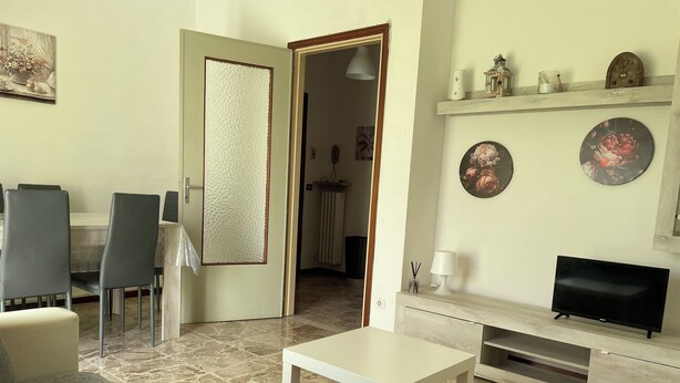 A living room with a sofa, a coffee table, a TV, a dining area with chairs, and a kitchen visible in the background. - La Casa Nel Verde - Two Bedroom Apartment, Sleeps 4 (Mede)