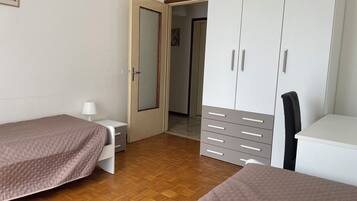 A bedroom with two beds, a wardrobe, a desk, and a chair.