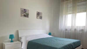 A bedroom with a bed, white nightstands, teal lamps, and two wall-mounted pictures. - La Casa Nel Verde - Two Bedroom Apartment, Sleeps 4 (Mede)