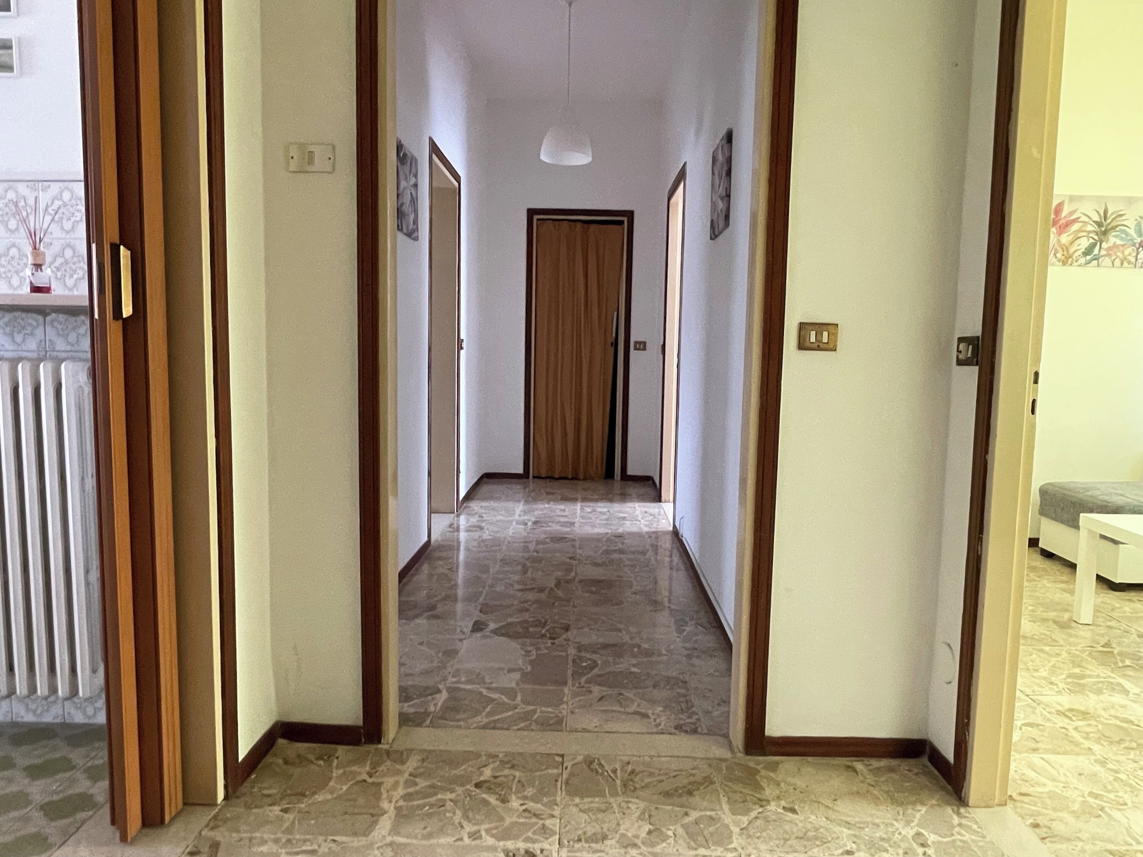 A hallway with a tiled floor, wooden doors, and a light fixture on the ceiling.