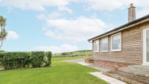 A house with a grassy yard, a stone wall, and a wooden deck. - The Dairy (Newton Stewart)