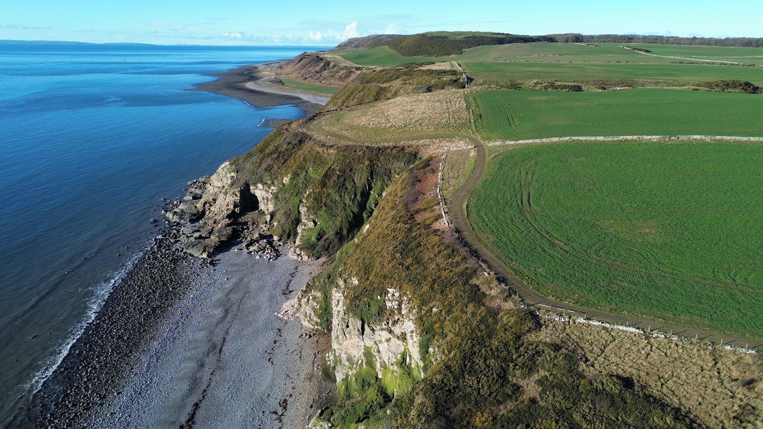 A coastal landscape with a rocky shoreline, green fields, and a clear sky.