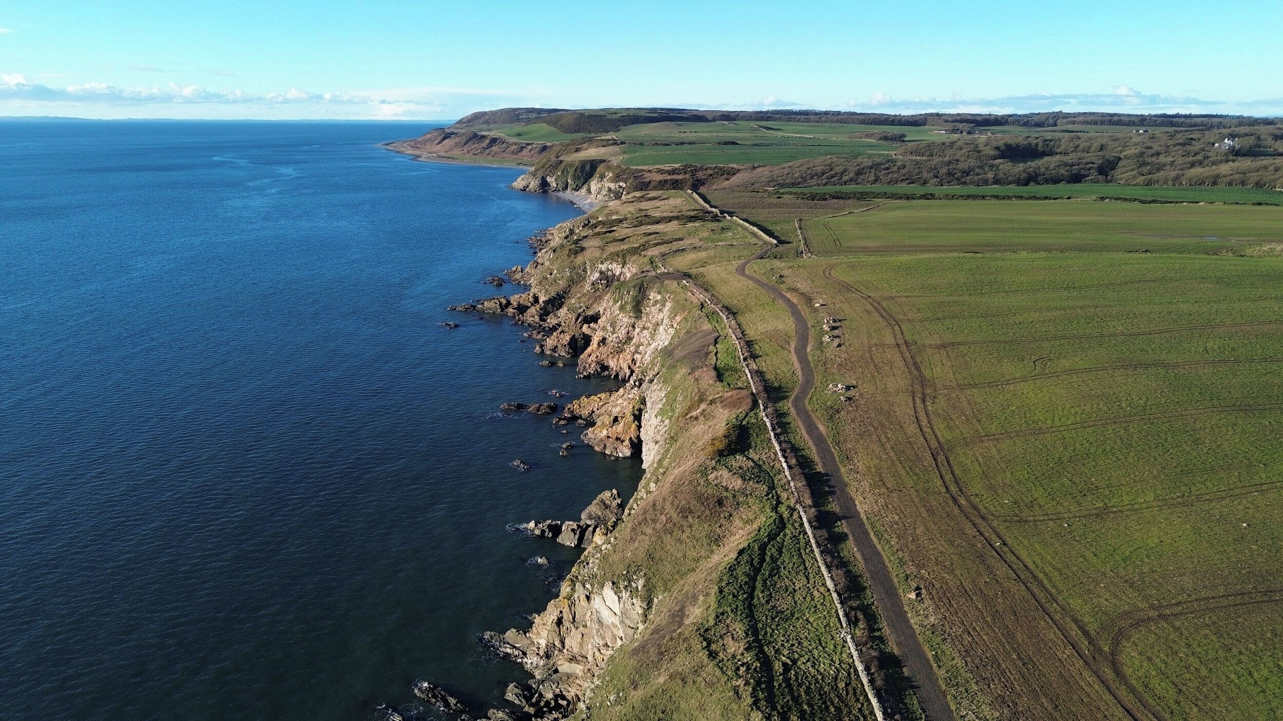 An aerial view of a coastal area with a narrow road along the cliffside, leading to a small settlement.