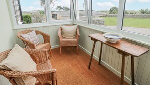 A cozy room with wicker chairs and a table, large windows offering a view of the countryside. - The Dairy (Newton Stewart)