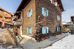 Ein hölzernes Gebäude mit blauen Fensterläden, einer Steintreppe und einem verschneiten Untergrund.