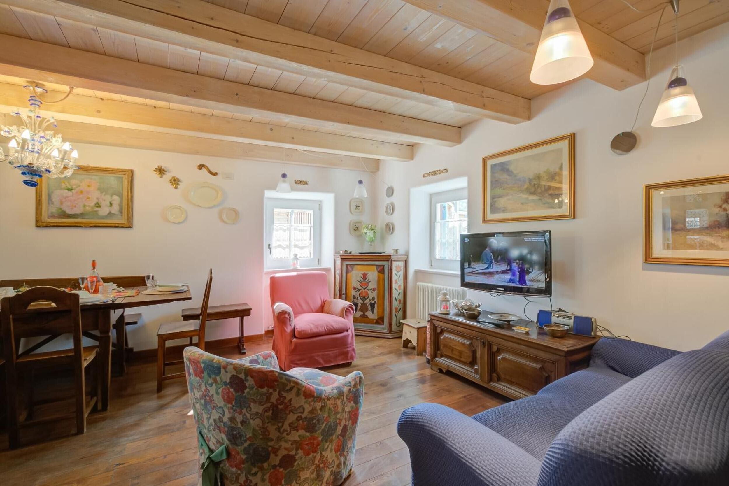 Een woonkamer met houten vloer, een televisie, een bank, een eettafel met stoelen en een kroonluchter.