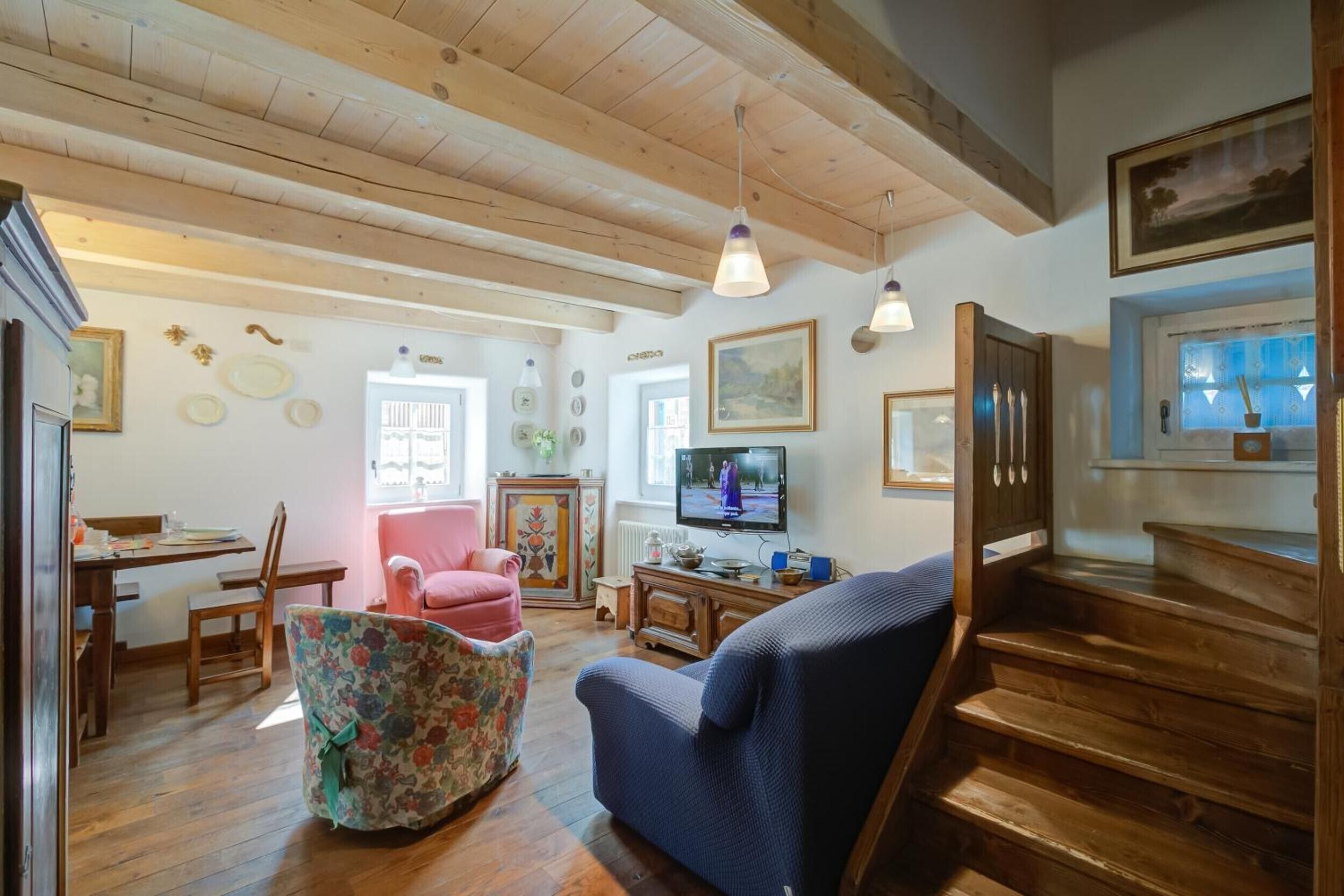 A living room with wooden floors, a blue sofa, a pink chair, a television, and a staircase.
