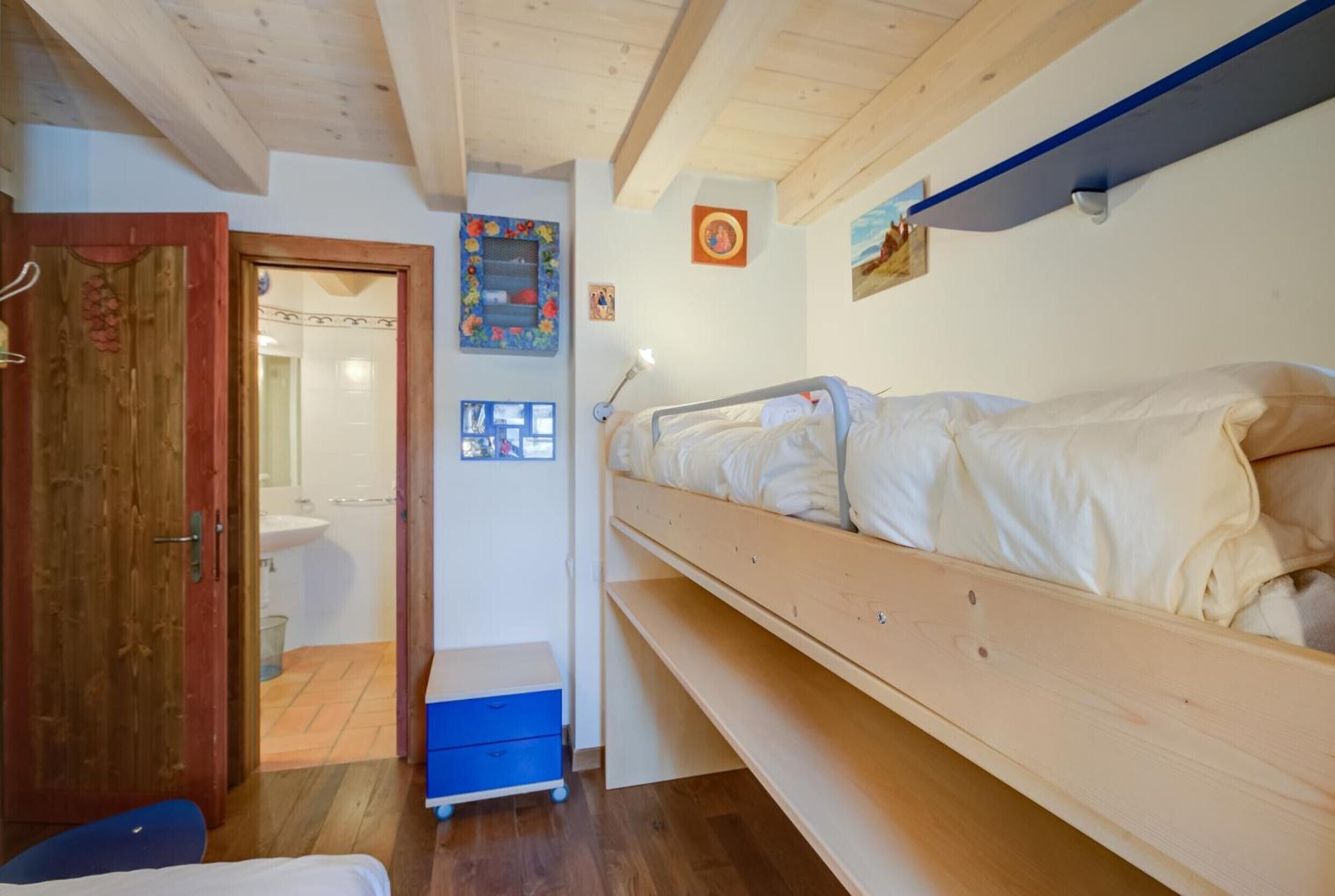 Een kamer met een stapelbed, een houten deur, een klein bureau met stoel, en een badkamer die door een open deur zichtbaar is.