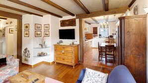 A living room with wooden beams, a television, a wooden cabinet, a sofa, and a dining area with chairs and a table. - Apartment 'Chalet San Valentino' with Mountain View, Shared Garden and Wi-Fi (Livigno)