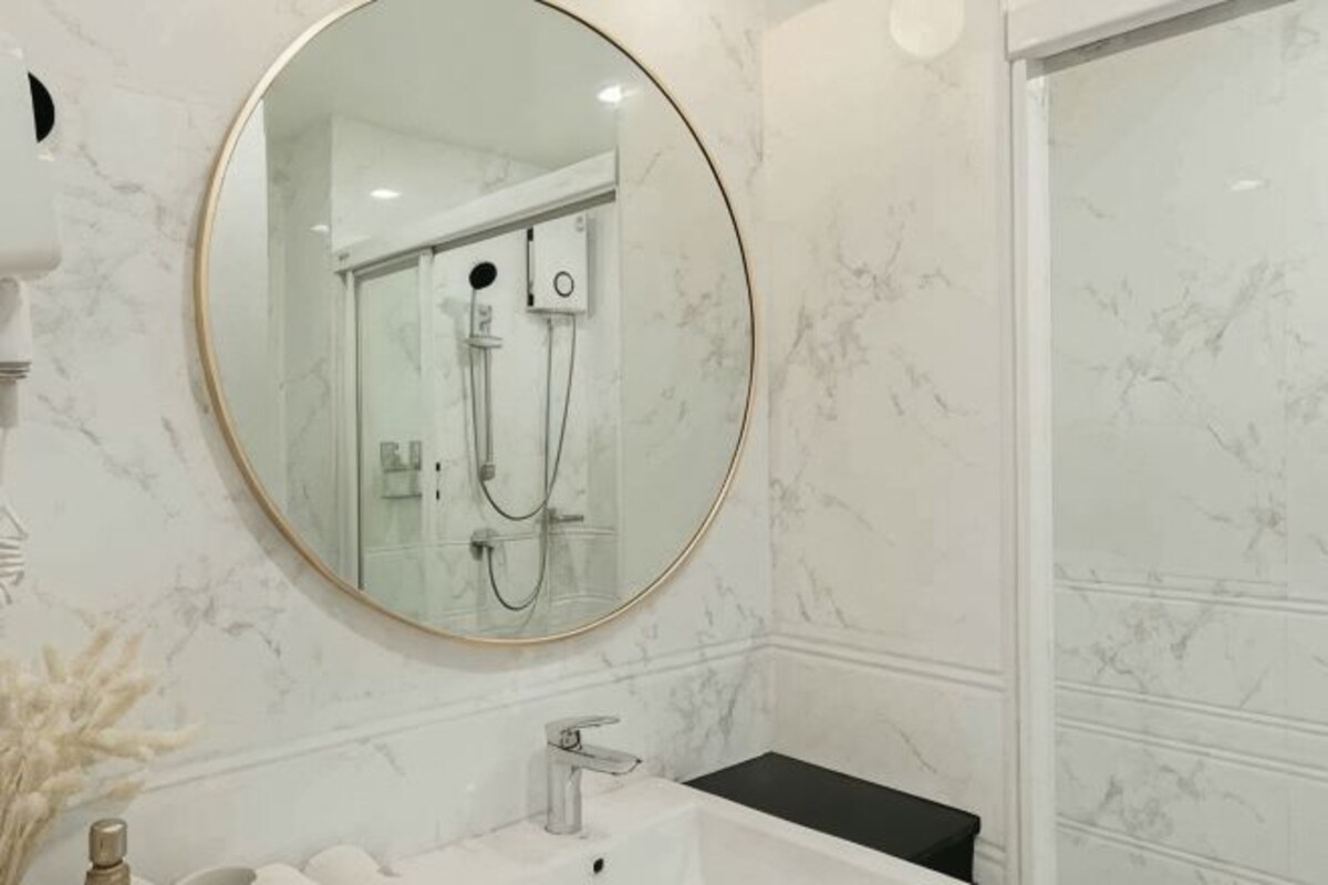 A bathroom with a round mirror, a white sink, and a shower area.