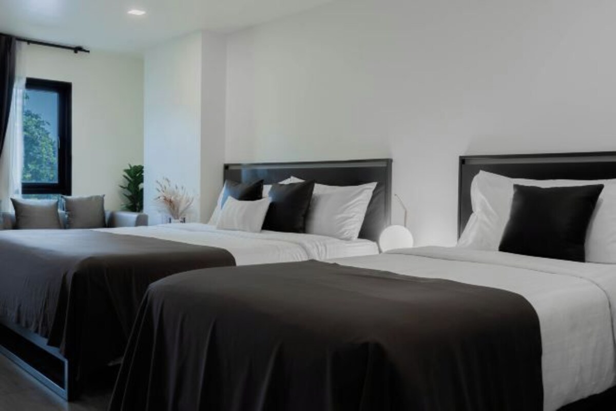 A hotel room with two beds, a nightstand, a window with curtains, and a plant.