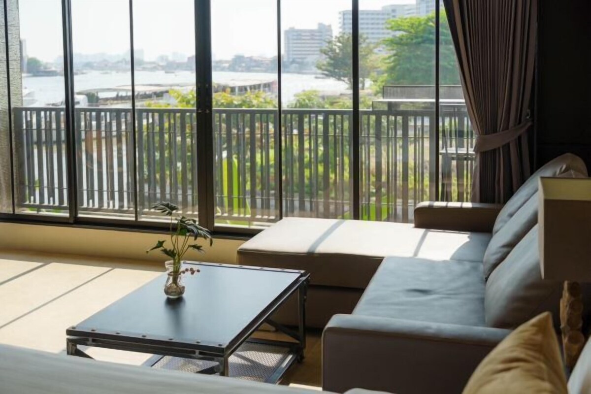 A room with a large window, a sofa, a small table, and a potted plant.
