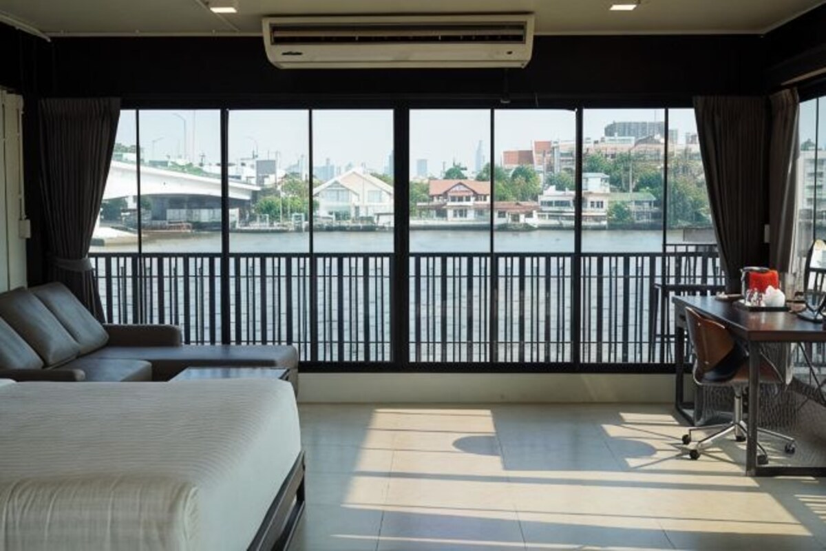 A hotel room with a bed, a desk, and a view of a cityscape through large windows.