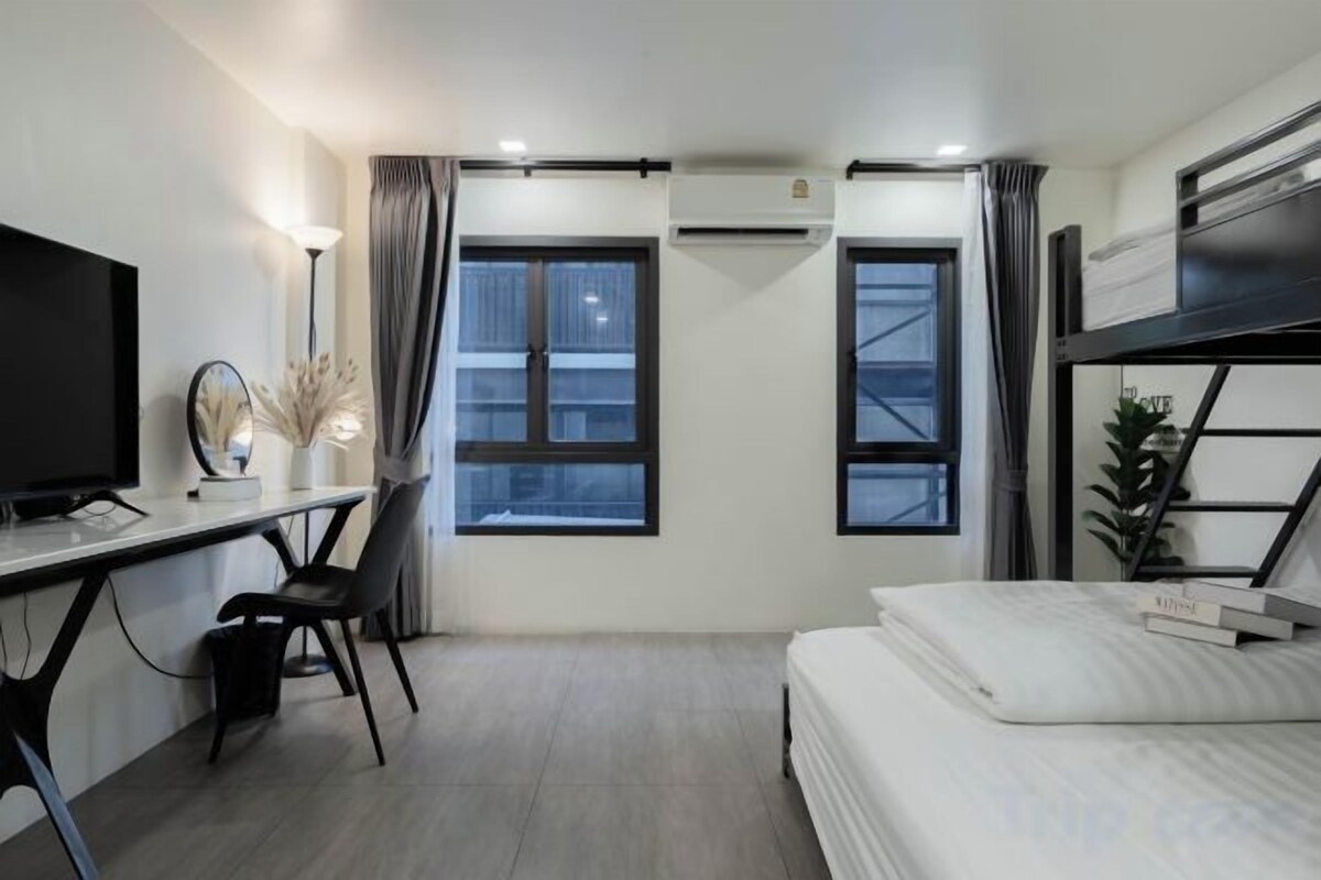 A hotel room with a bed, a desk with a computer, a television, and two windows with curtains.
