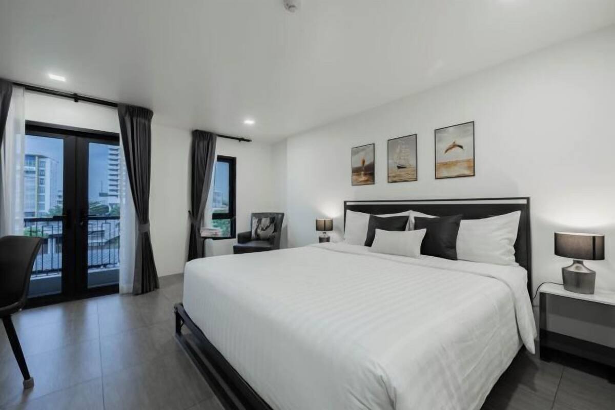 Habitación de hotel moderna con una cama grande, una silla, una mesita de noche y vistas a la ciudad desde un balcón.